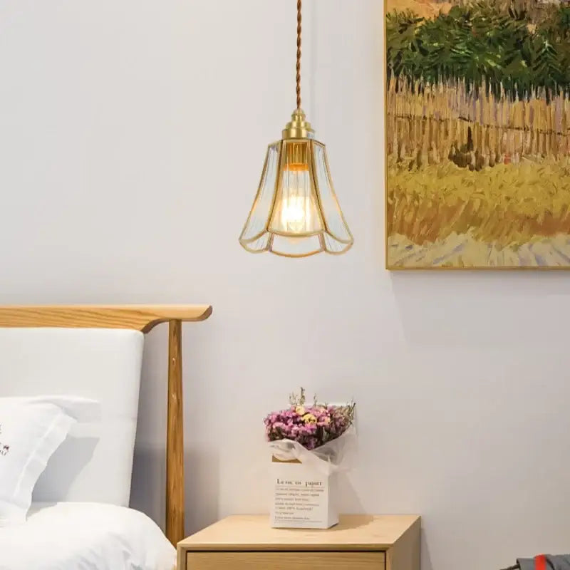 A minimalist brass-framed glass led hanging pendant light with braided cord above a wooden nightstand