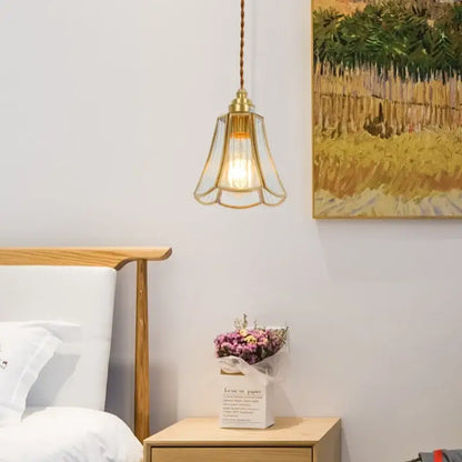A minimalist brass-framed glass led hanging pendant light with braided cord above a wooden nightstand