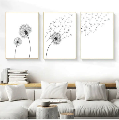 Three minimalist dandelion black-and-white canvas wall art prints with thin gold frames above a white sofa by DecorBites