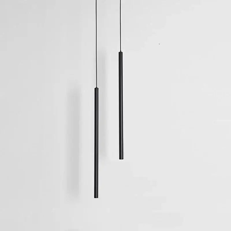 Two sleek black cylindrical decorbites black slim led pendant lamps hang vertically against a plain white background