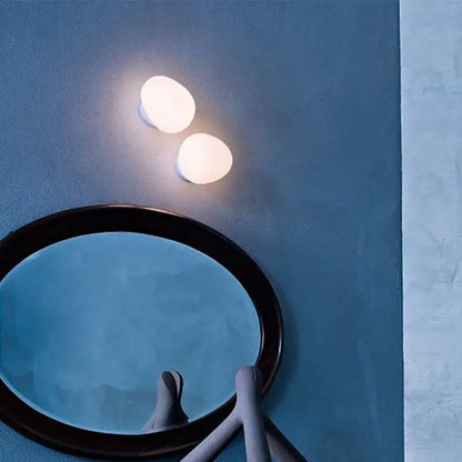 Two warm oval-shaped minimalist frosted glass decorbites cobblestone wall lamps on a cool blue wall for living room decor