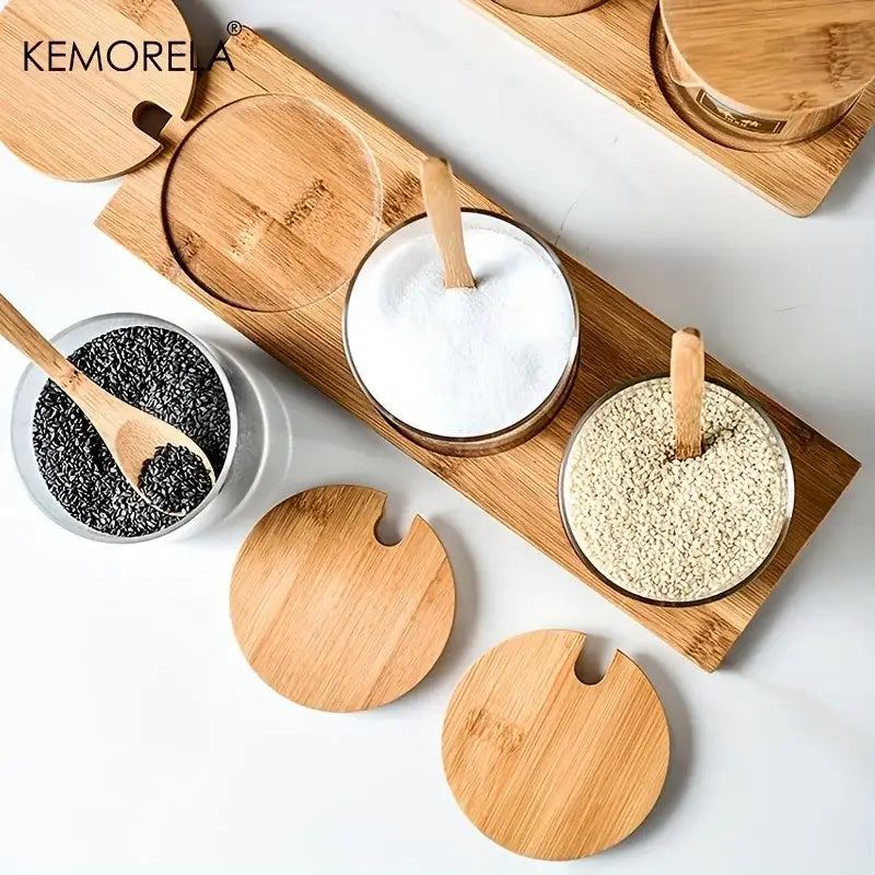 Minimalist glass spice jar set with bamboo lids and wooden spoons arranged on a matching bamboo tray for kitchen organization