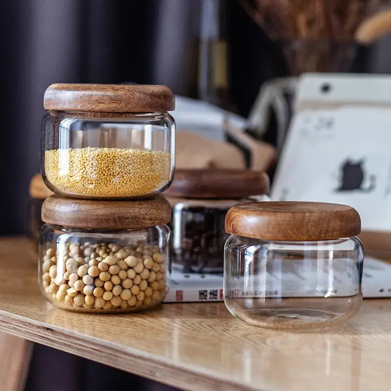 Minimalist clear glass spice jars with smooth rounded acacia wood lids for kitchen storage on countertop