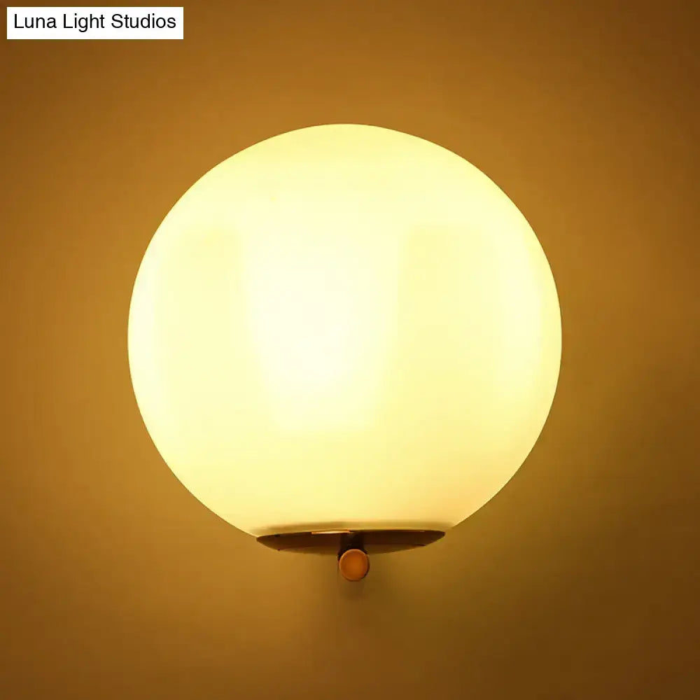 Minimalist bedroom wall sconce with warm white light featuring frosted white glass ball and brass-finished mounting hardware