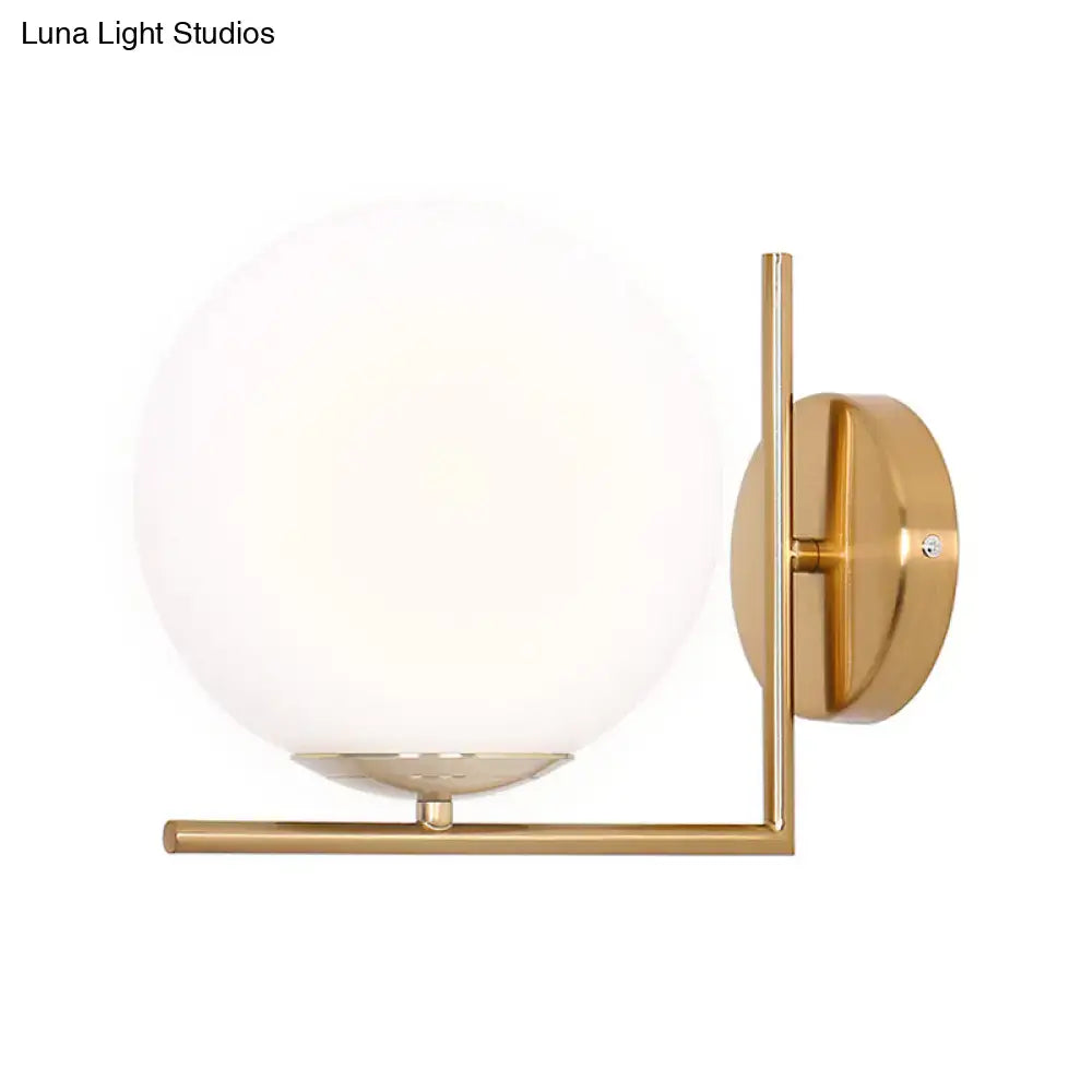 Minimalist gold wall sconce with frosted white glass ball providing warm white light for bedroom lighting