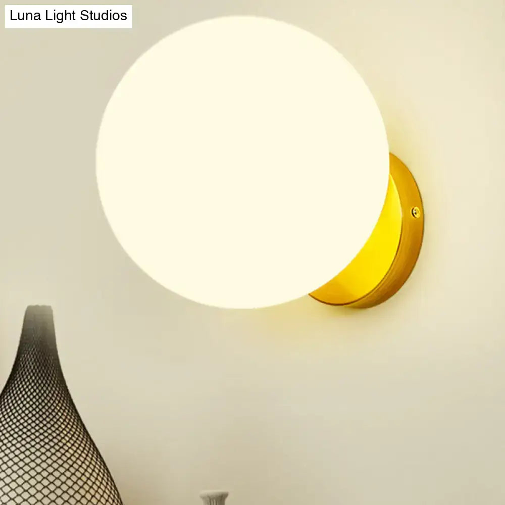 A minimalist gold and white glass ball bedroom wall light with a frosted white glass ball shade and metal base