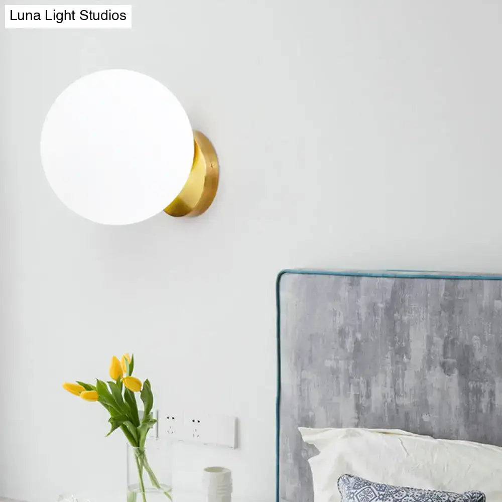 Minimalist gold and white glass ball sconce with frosted white glass globe and polished brass base for bedroom wall light