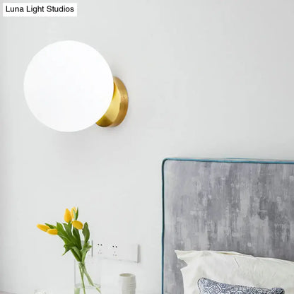 Minimalist gold and white glass ball sconce with frosted white glass globe and polished brass base for bedroom wall light