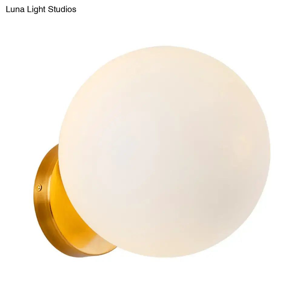 Minimalist gold wall sconce featuring a sleek spherical frosted white glass ball for bedroom lighting