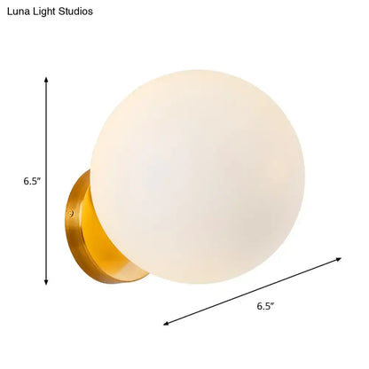 Minimalist gold and white glass ball sconce with frosted white glass ball and polished brass backplate for bedroom walls