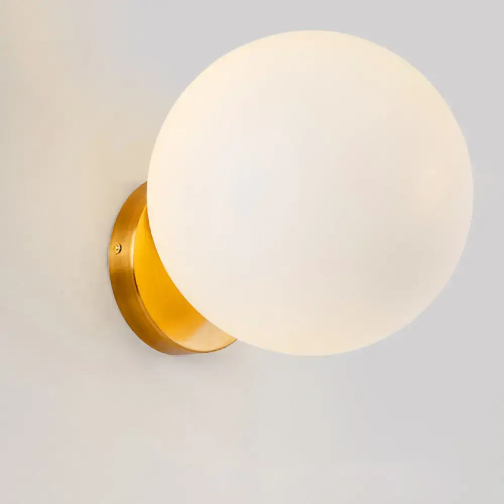 Minimalist gold wall sconce with a sleek frosted white glass ball for bedroom lighting