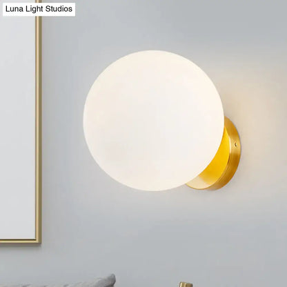 Minimalist gold and white bedroom wall sconce with a frosted white glass ball and polished metal base
