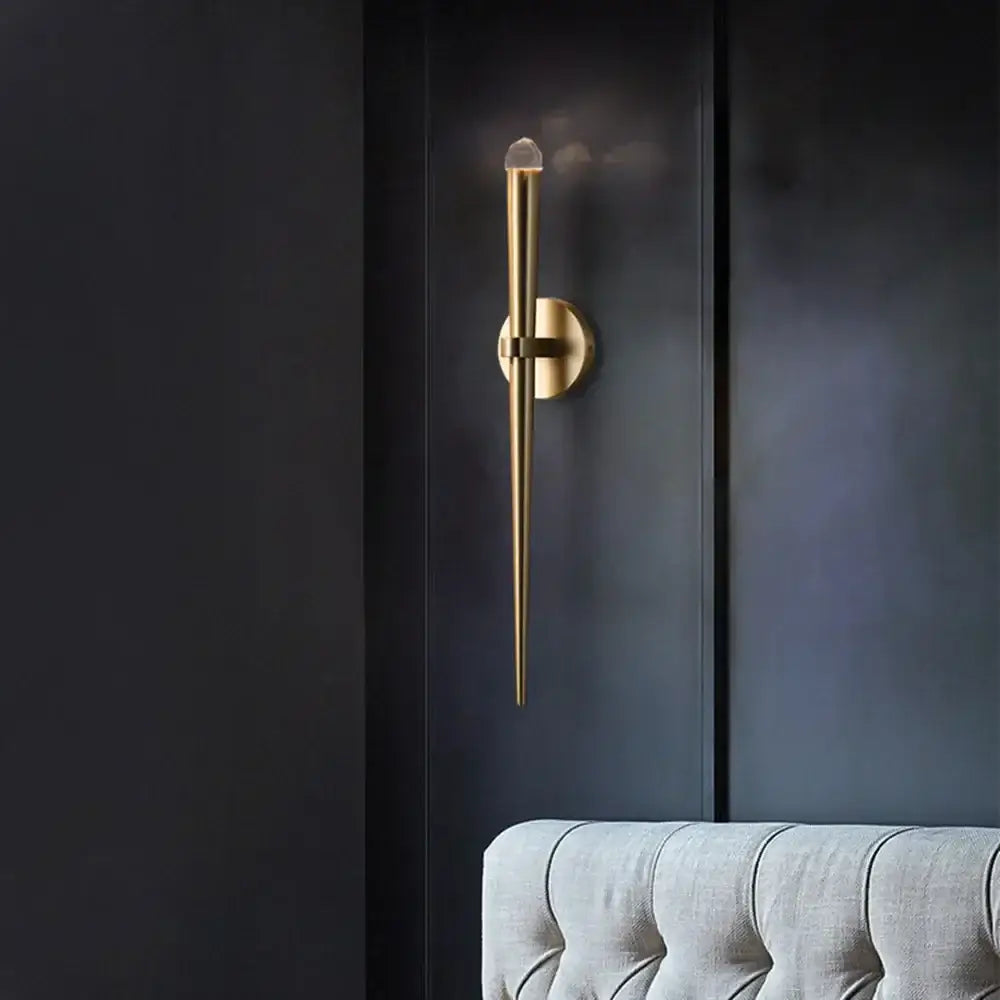 A sleek gold wall sconce with a tapered design and clear crystal accent for decorbites crystal minimalist decor
