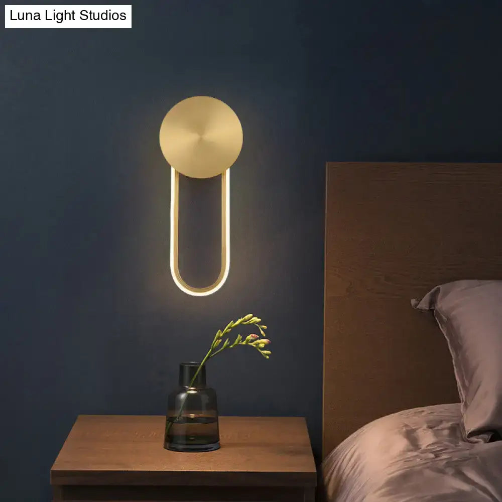 Minimalist gold wall sconce light with illuminated u-shaped frame and circular top plate for bedroom lighting