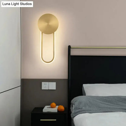Minimalist gold wall sconce light with elliptical shape and u-shaped body emitting soft ambient light for bedroom