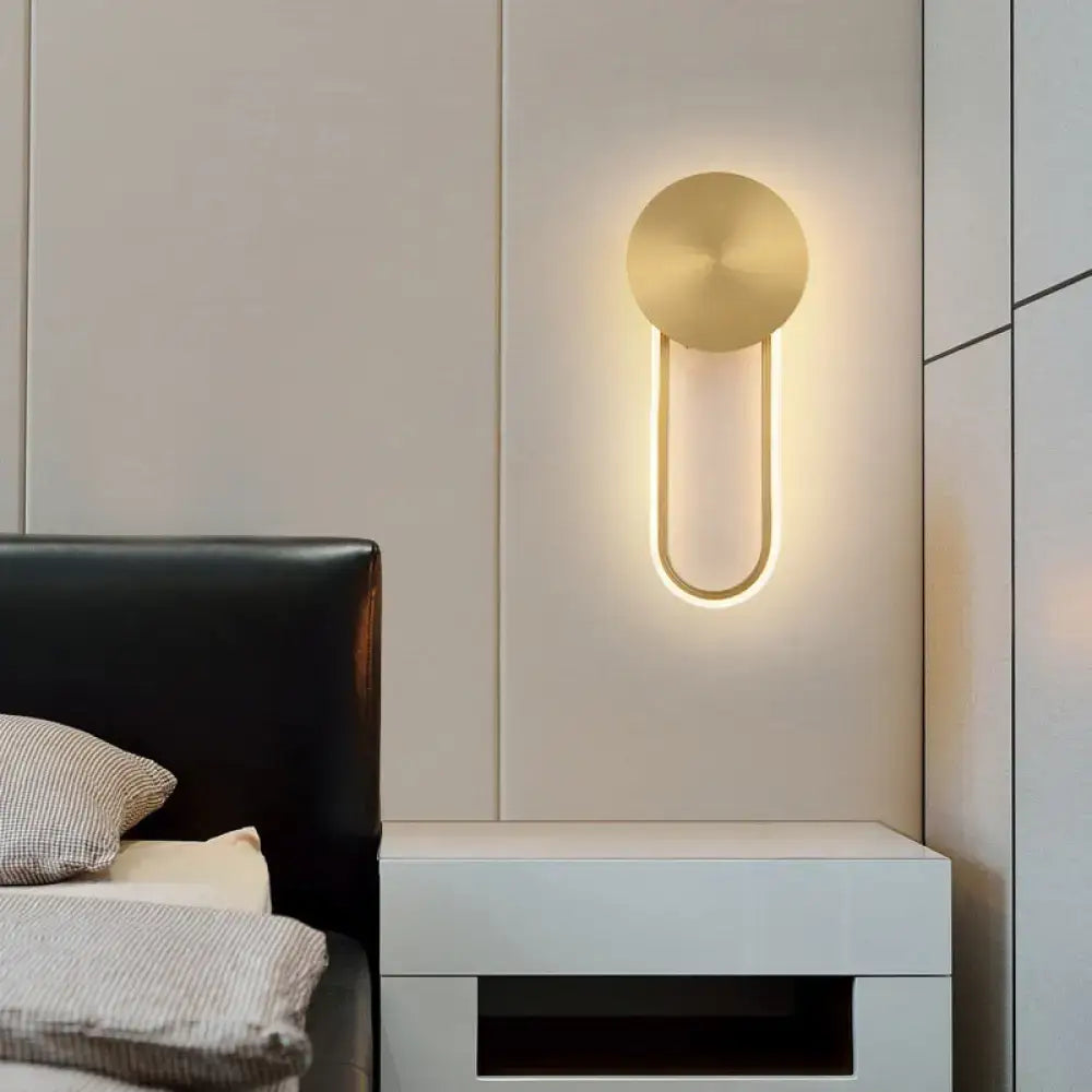 Minimalist gold elliptical wall sconce light with a circular top and illuminated u-shaped base for bedroom use