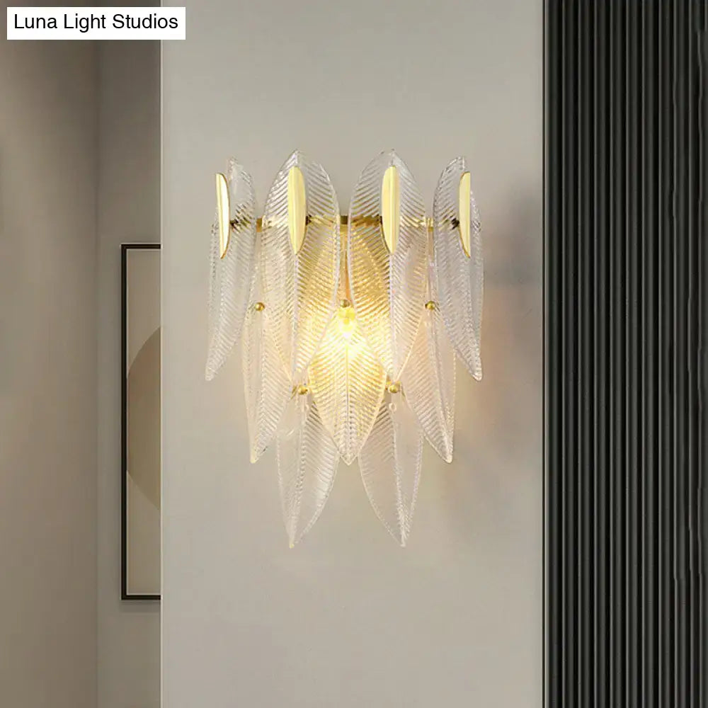 Minimalist wall sconce with clear leaf-shaped glass and gold finish metal accents for bedroom lighting