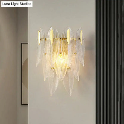 Minimalist wall sconce with clear leaf-shaped glass and gold finish metal accents for bedroom lighting