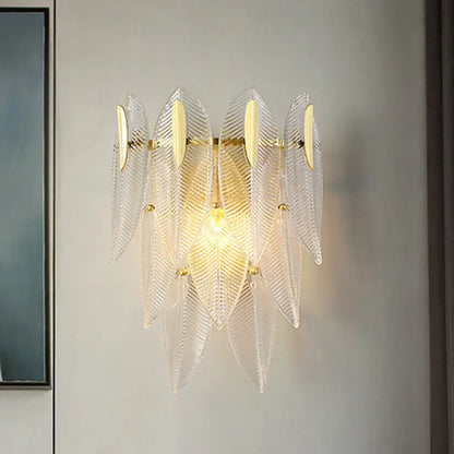 Minimalist wall sconce with clear glass feather shape and gold finish metal accents for bedroom lighting