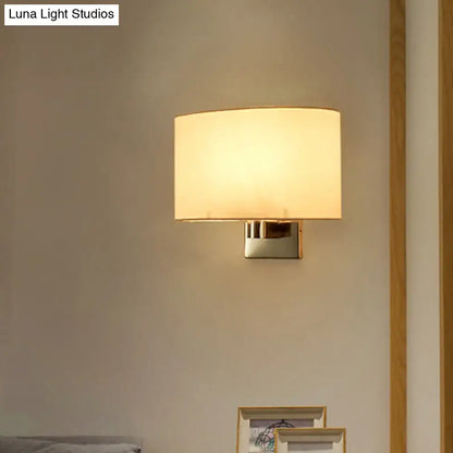 Modern wall-mounted lamp with a soft, warm glow from its off-white fabric shade and sleek metallic base.