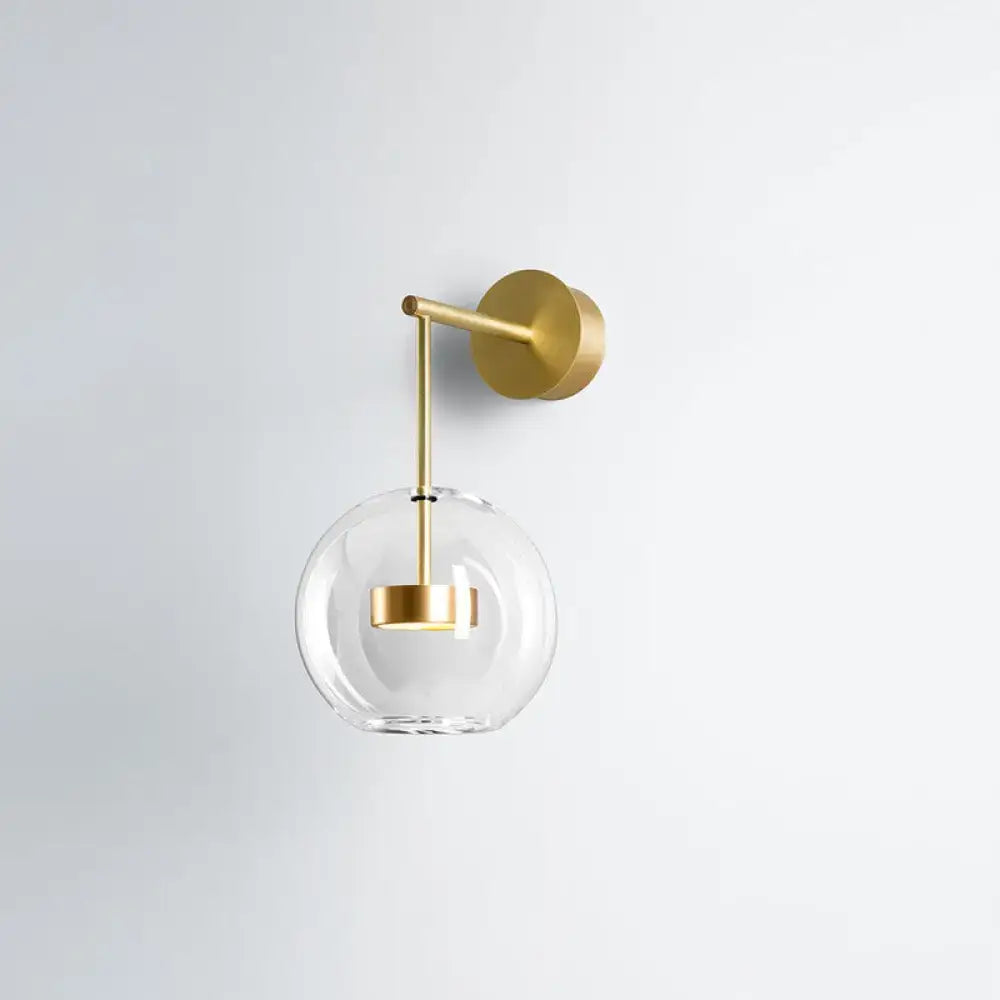 Minimalist gold-toned wall hanging light with clear glass globe and brass hardware for bedroom sconce lighting