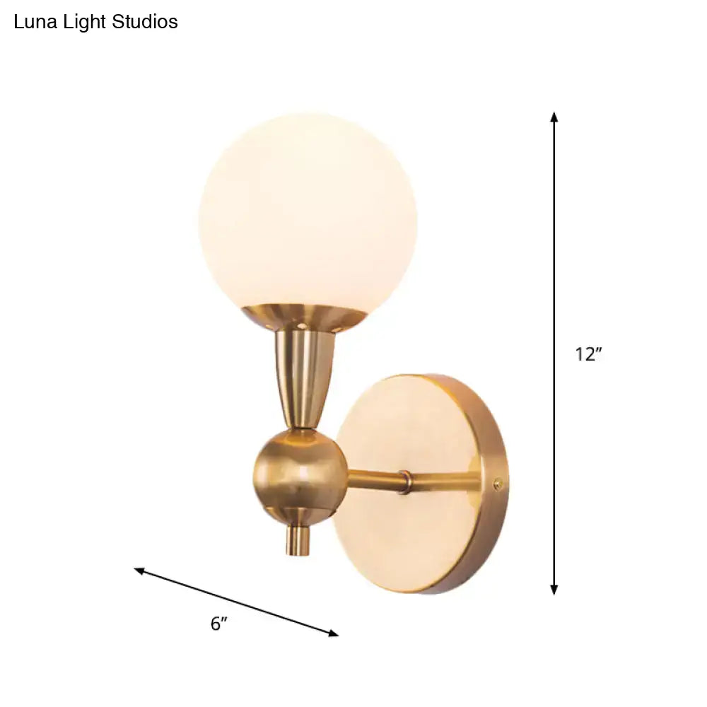 Minimalist brass-finished wall sconce with frosted hand blown glass globe shade for bedroom sconce light