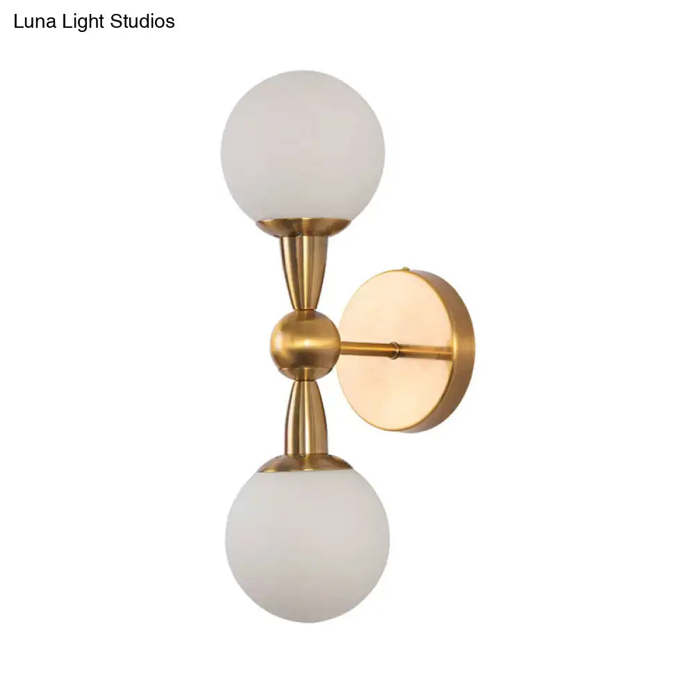 Brass-finished minimalist gold hand blown glass wall sconce with two frosted globe shades for bedroom lighting