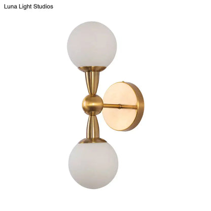 Brass-finished minimalist gold hand blown glass wall sconce with two frosted globe shades for bedroom lighting