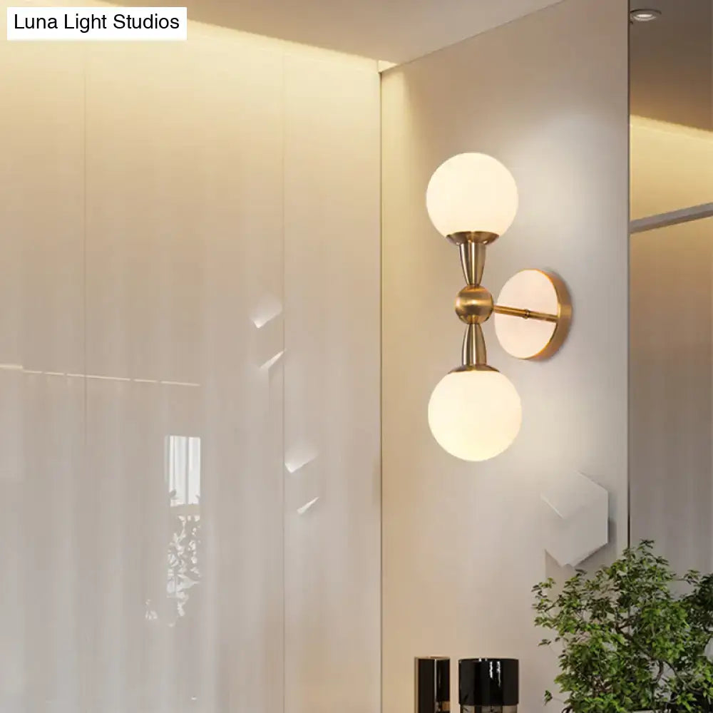 Brass-finished minimalist wall sconce light with two frosted hand blown glass globe shades for bedroom use