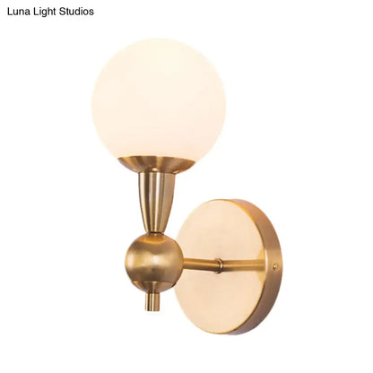 Brass-finished minimalist wall sconce with hand blown frosted glass globe shade for bedroom sconce light