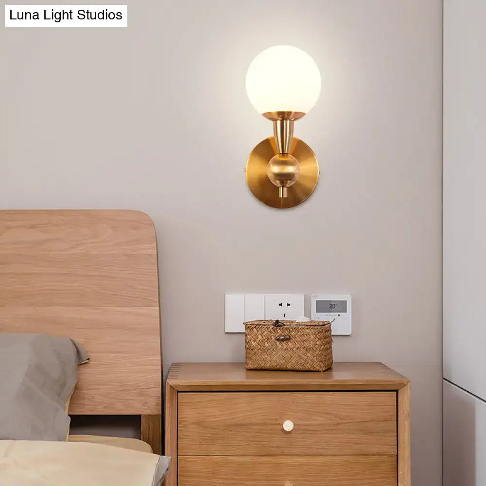 Minimalist gold wall sconce light featuring hand blown glass with a frosted globe shade for bedroom use