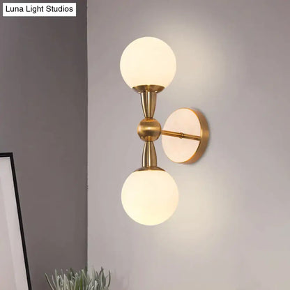 Minimalist gold hand blown glass wall sconce with two frosted globe shades for elegant bedroom lighting