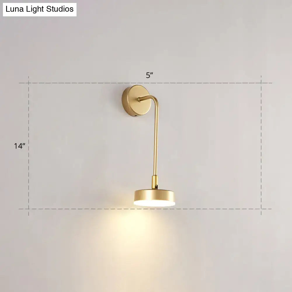 Minimalist gold metal led sconce wall mounted lamp with slender curved arm and circular base emitting warm ambient light