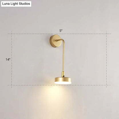 Minimalist gold metal led sconce wall mounted lamp with slender curved arm and circular base emitting warm ambient light