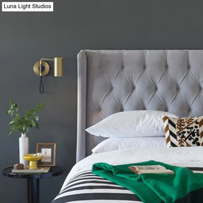 Minimalist gold metal wall lamp bedside spotlight with bulb base mounted near gray tufted velvet headboard
