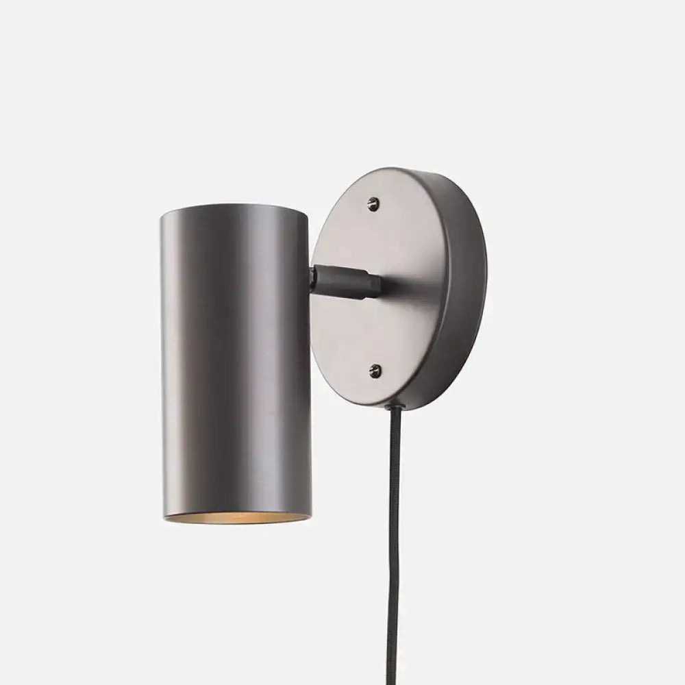 Matte-finished dark gray cylindrical bedside spotlight wall lamp with circular backplate and black cord bulb base