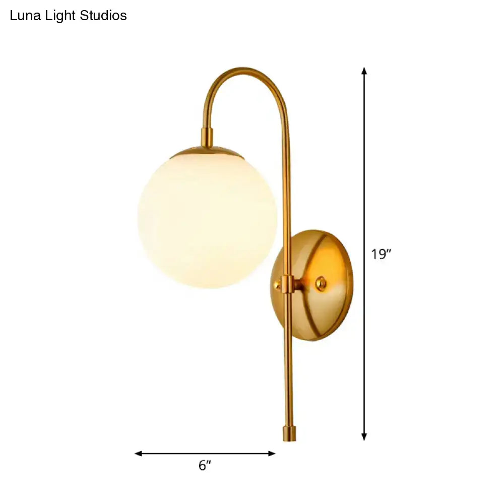 Brass-finished gold mini globe wall sconce with curved arm and frosted glass globe for minimalist bedroom lighting
