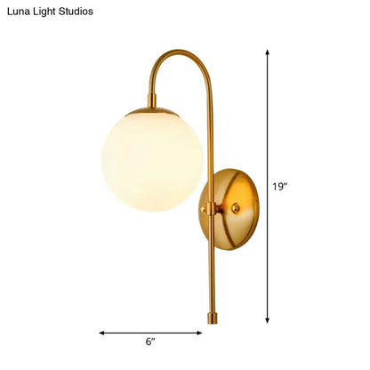 Brass-finished gold mini globe wall sconce with curved arm and frosted glass globe for minimalist bedroom lighting