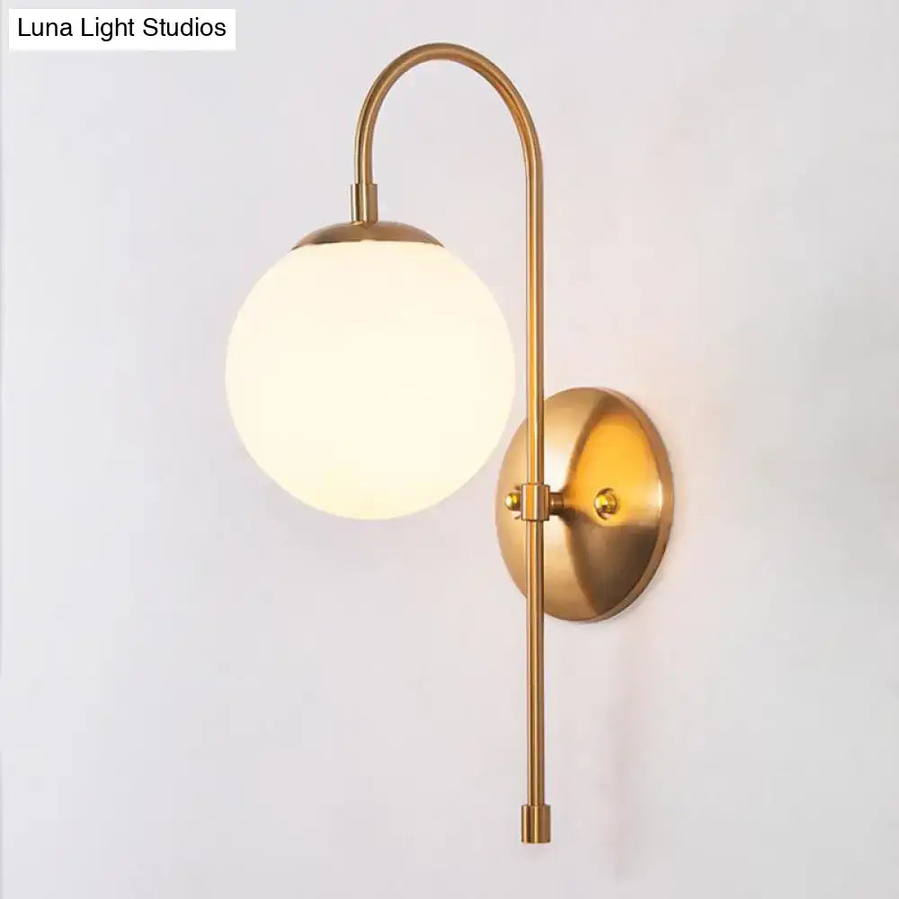 Brass-finished gold mini globe wall sconce with a spherical frosted glass globe for minimalist bedroom lighting