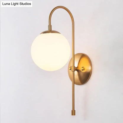 Brass-finished gold mini globe wall sconce with a spherical frosted glass globe for minimalist bedroom lighting