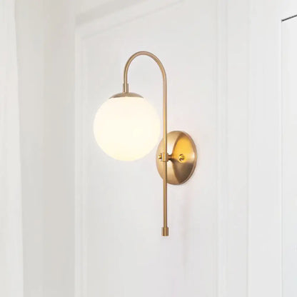 A sleek minimalist gold mini globe wall sconce with a curved brass arm and frosted glass globe shade for bedroom lighting
