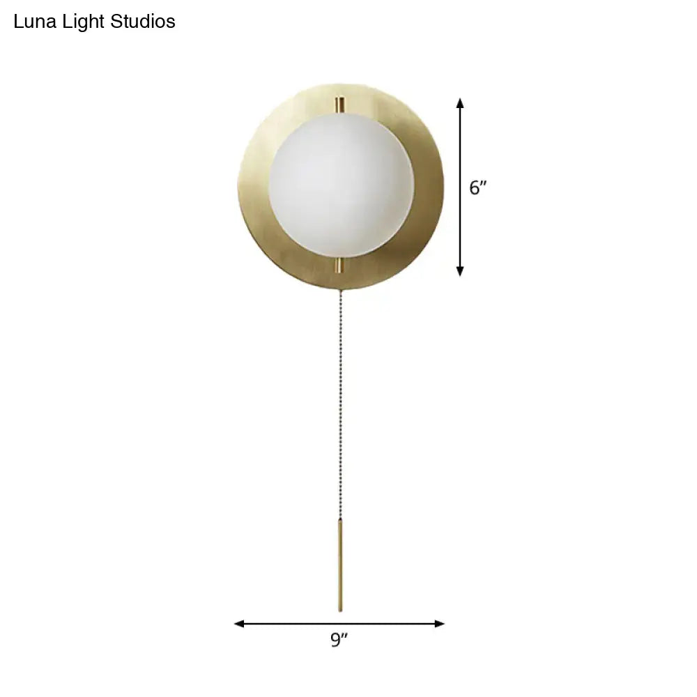 A sleek minimalist gold mini globe wall sconce with brass finish frosted glass globe and elegant chain pull for bedroom lighting