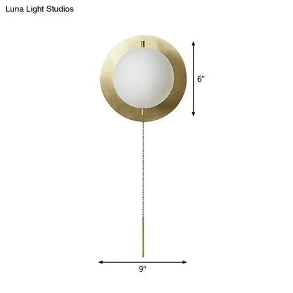 A sleek minimalist gold mini globe wall sconce with brass finish frosted glass globe and elegant chain pull for bedroom lighting