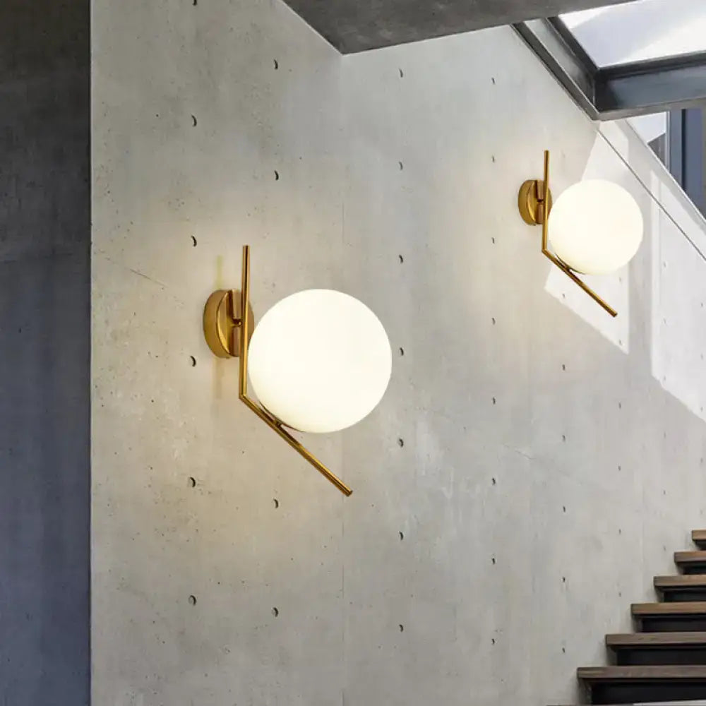 Minimalist gold mini globe wall sconce with a spherical frosted glass globe and geometric arm for bedroom lighting