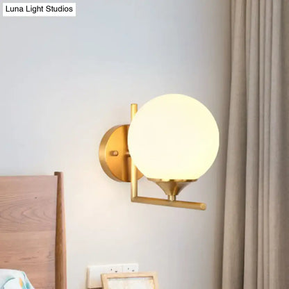Minimalist gold toned wall mounted light with frosted glass globe and metal arm for bedroom wall mounted use
