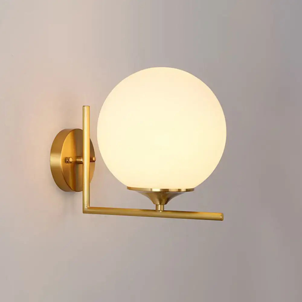 Minimalist gold-toned wall mounted light with frosted glass globe and metal arm for bedroom use