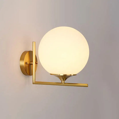 Minimalist gold-toned wall mounted light with frosted glass globe and metal arm for bedroom use