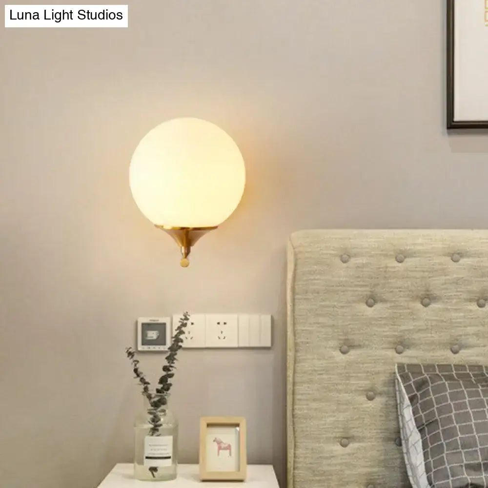 Minimalist gold sphere wall mounted light with warm frosted glass globe and brass finished base for bedroom use