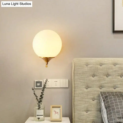 Minimalist gold sphere wall mounted light with warm frosted glass globe and brass finished base for bedroom use