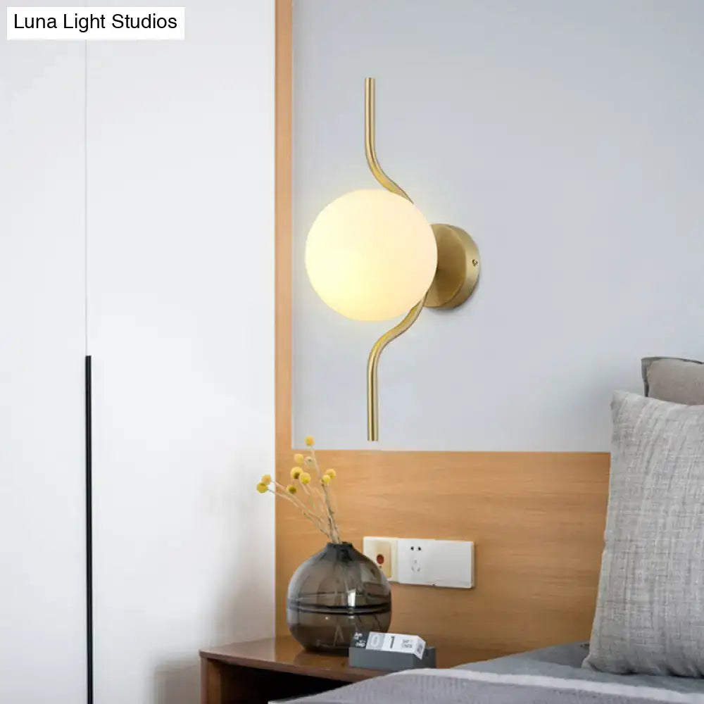 Minimalist gold sconce light with a curved gold arm and frosted white globe shade for bedroom wall light